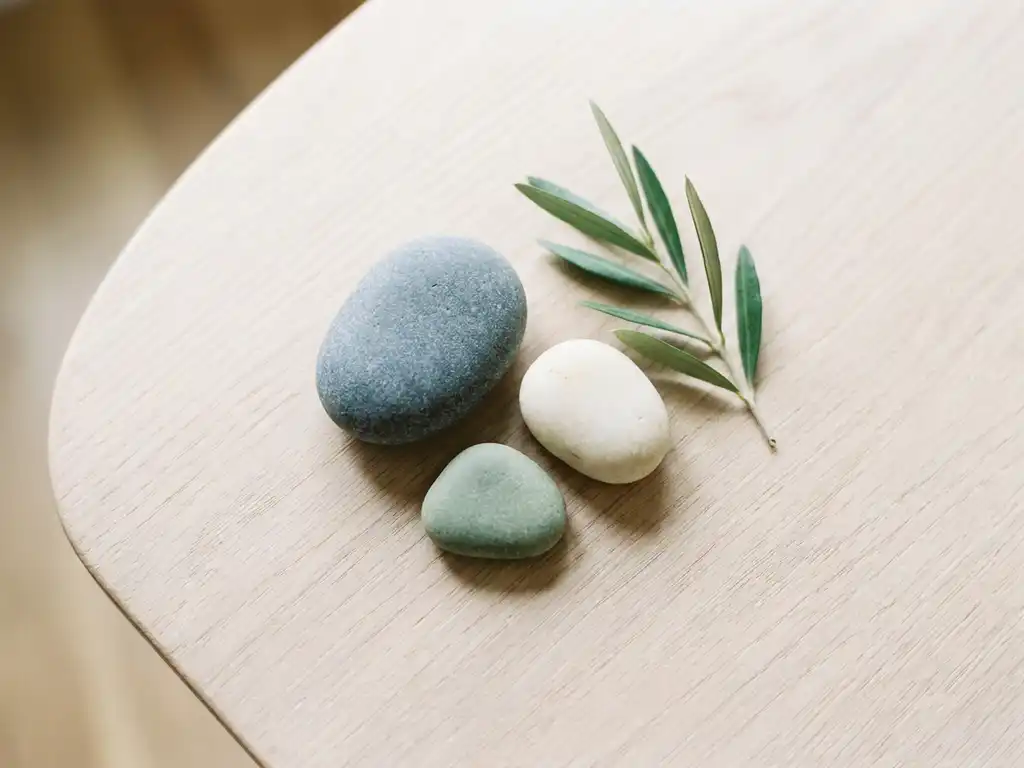 Drie grijze rivierkeien in driehoeksformatie op een wit eikenhouten bureau, met een groen plantentakje ernaast.